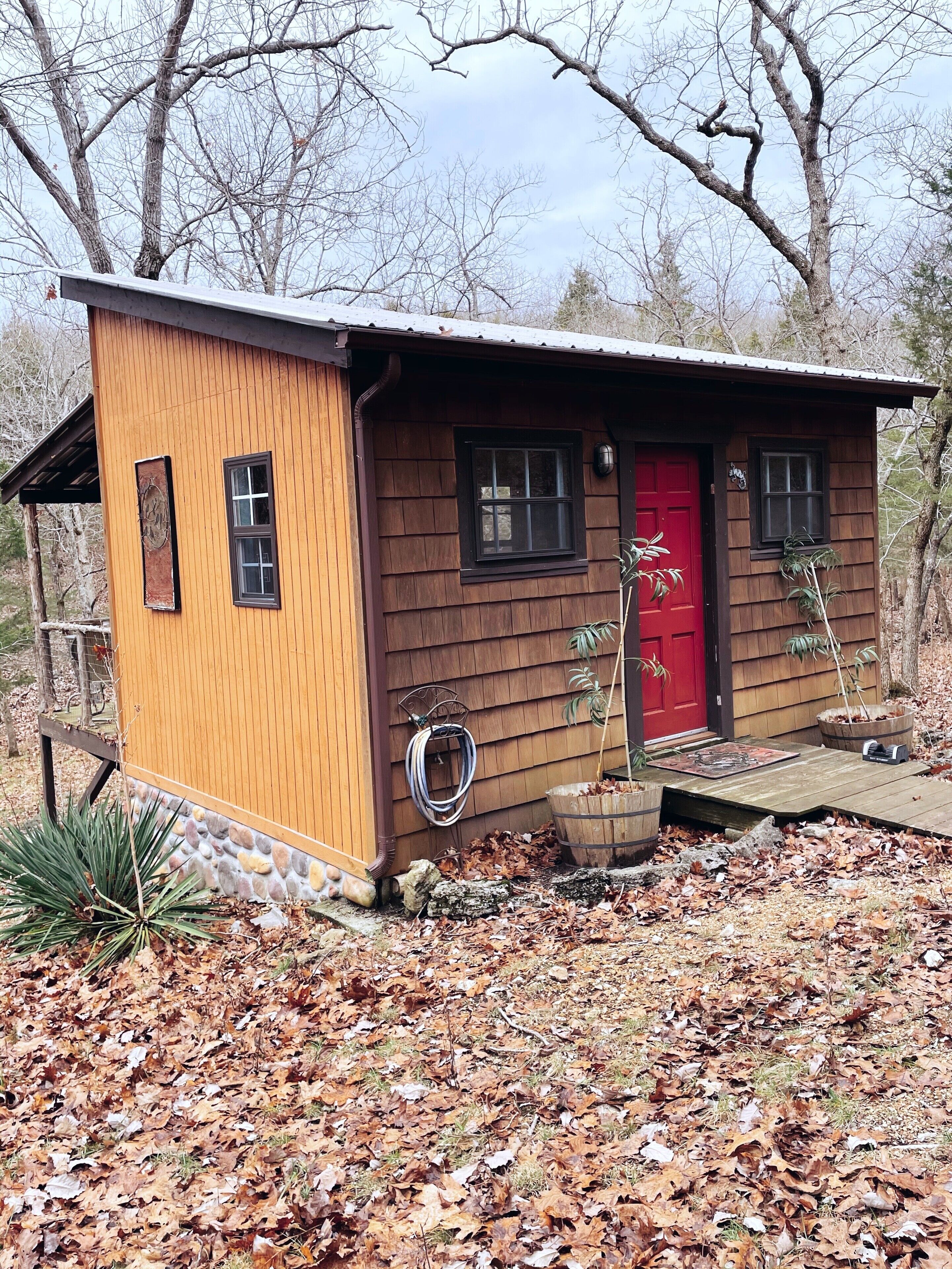 A small wooden cabin with a red door, two windows, and a porch area.