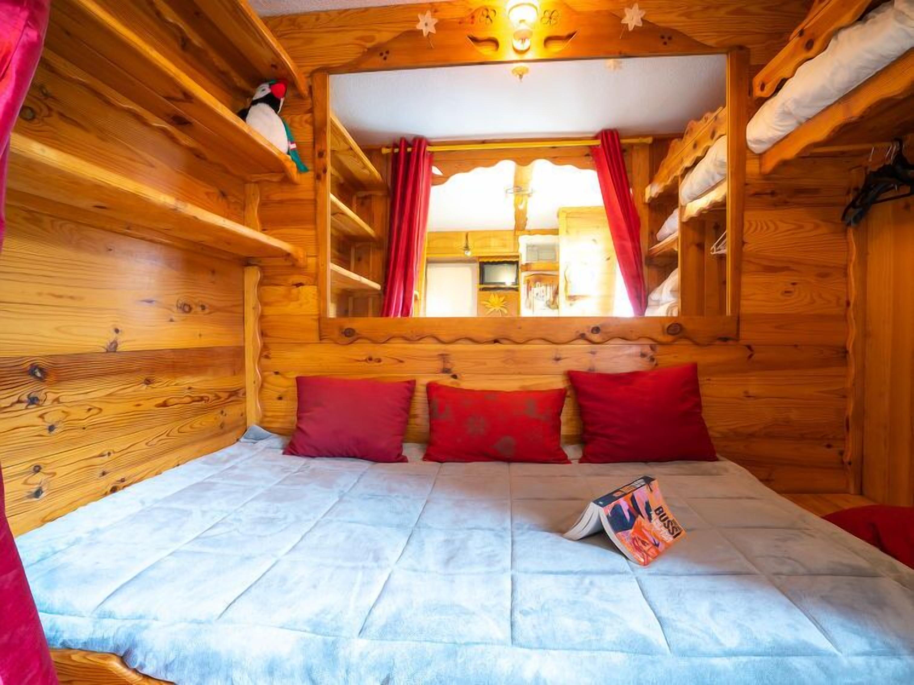 Acogedora habitación de cabaña de madera con cama, almohadas rojas y ventana con cortinas.