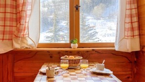 A cozy cabin interior with a breakfast setup on a wooden bench by a window overlooking a snowy landscape. - Soyouz Vanguard by Interhome (Le Corbier)