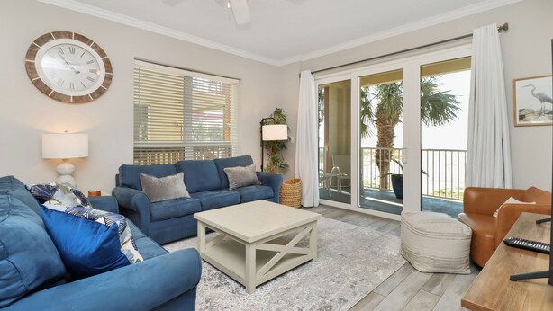 A living room with a blue sofa, a white coffee table, and a ceiling fan. - Great Views, Rooftop Pool, Hot Tub & Sauna ~ Summerhouse 106 (Mexico Beach)
