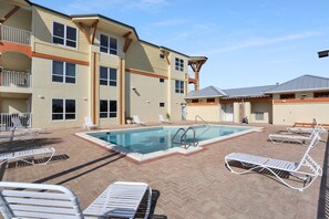A pool area with lounge chairs and a building with multiple balconies.
