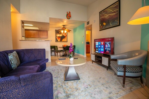 A modern living room with a sofa, a coffee table, a TV, and a dining area. - Cozy 2 bedroom condo near Strip (Las Vegas)