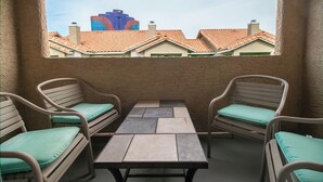 Een balkon met twee rieten stoelen en een tafel, met uitzicht op gebouwen met rode pannendaken.