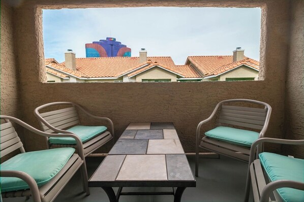 Ein Balkon mit zwei Korbstühlen und einem Tisch, der einen Blick auf Gebäude mit roten Ziegeldächern bietet.