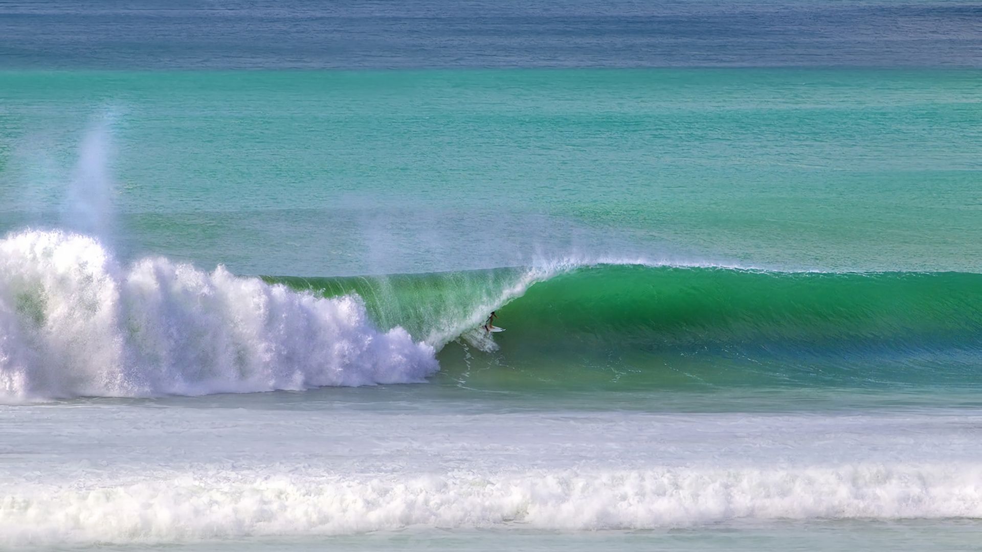 Eine große Welle im Meer, auf der ein Surfer reitet.