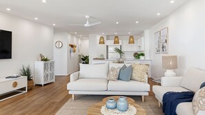 Una sala de estar moderna con un sofá blanco, una mesa de centro con objetos decorativos, un televisor y un ventilador de techo.