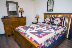 A bedroom with a wooden bed, a dresser, a mirror, and a window. - One bedroom condo, walking distance to Estes Park, river view from deck. (Estes Park)