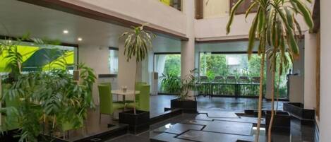 A spacious indoor area with multiple seating arrangements, potted plants, and a balcony with a view.