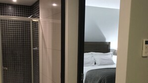 A hotel room with a shower, a bed, and a bedside table. - Secure, Modern & Comfy, Lux Suite @77 Independence (Windhoek)