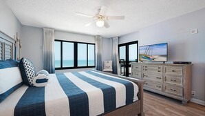 Quarto com cama, penteadeira, televisão e vista para o mar.