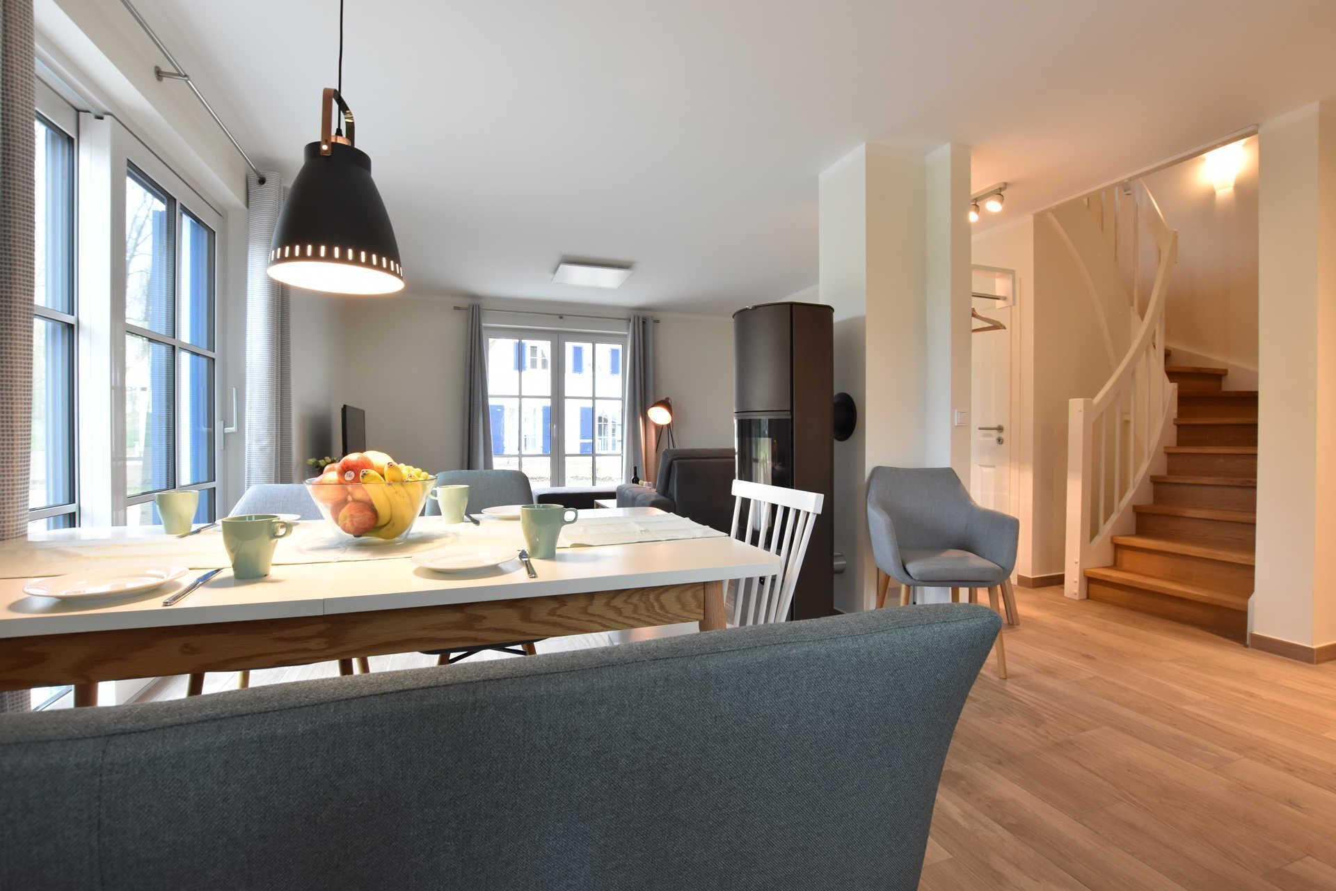 A modern kitchen with a dining table, chairs, and a fruit bowl. There is a staircase leading to another level.