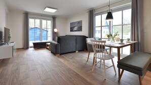 Ein modernes Wohnzimmer mit einem grauen Sofa, einem Esstisch mit Stühlen und einem Fernseher auf einem Schrank.
