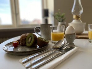A breakfast setting with a plate of toast, kiwi, and cherry tomatoes, a glass of orange juice, a cup, and a bowl of eggs.