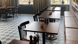 A restaurant interior with multiple tables and benches, pendant lighting, and large windows.