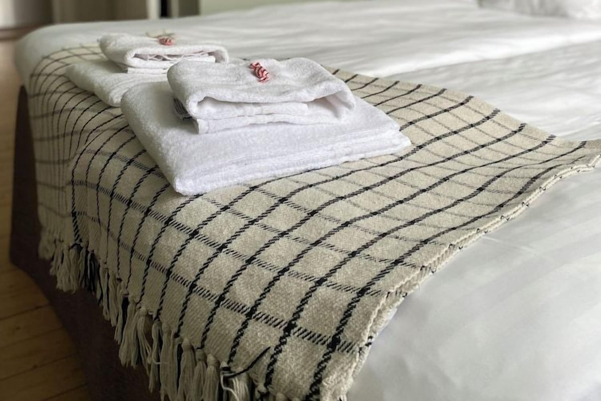 A neatly made bed with folded white towels and a checkered throw blanket.