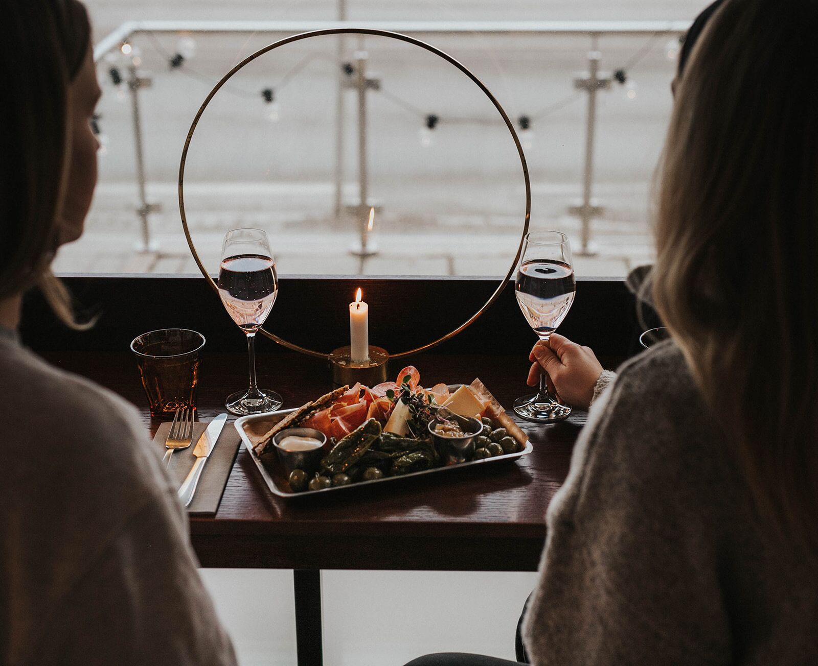 Two people seated at a table with a tray of food, glasses of wine, and a candle.