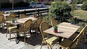 An outdoor seating area with wicker chairs and tables, large umbrellas, and a view of a street and buildings in the background.