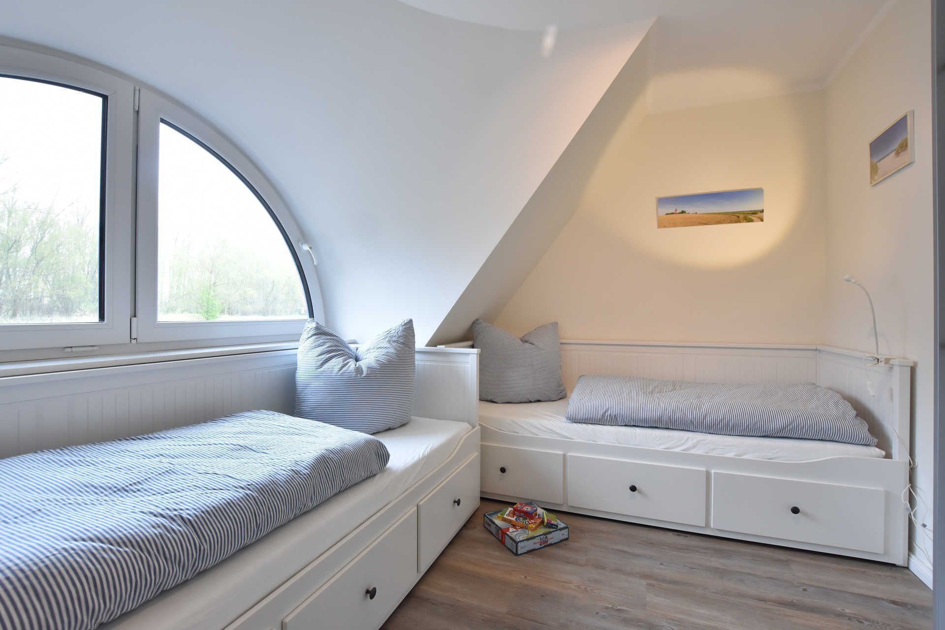 A bedroom with two beds, a window, and a painting on the wall.