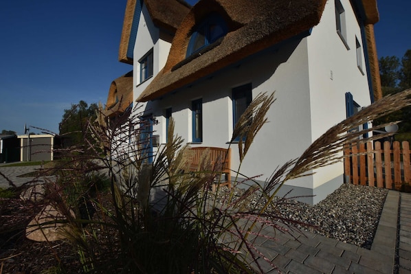 A modern house with a unique thatched roof, white exterior walls, and a wooden fence.