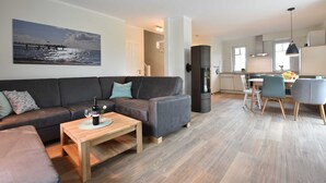 A modern living room with a sofa, coffee table, and a painting of a pier. - 4-room vacation home with fireplace (max. 6 persons) - left - L7 Holiday home (Rerik)