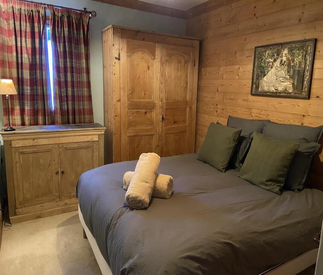 A bedroom with a bed, pillows, a wooden wardrobe, and a painting on the wall.
