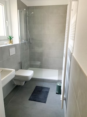Uma casa de banho moderna com chuveiro, sanita e lavatório.