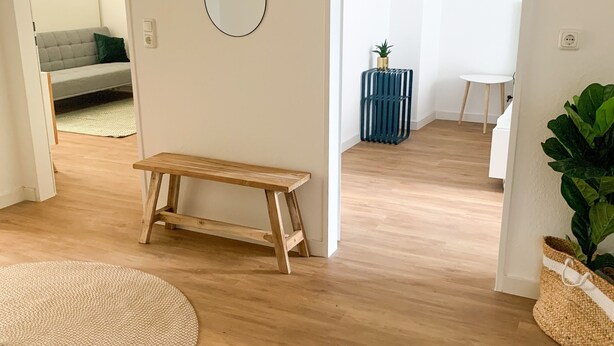 A spacious room with a wooden bench, a round rug, and a large mirror on the wall. - Glück Auf Appartement Lösortstraße (Duisburg)