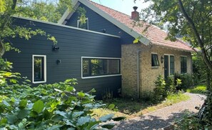 Ein zweistöckiges Haus mit dunkler Fassade und einem Backsteinbereich. Im oberen Stock befinden sich zwei Fenster und im unteren ein Eingang.