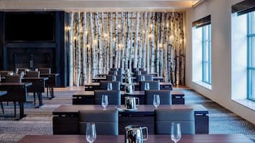 A modern restaurant with a long dining area, a fireplace, and a wall decorated with birch branches and lights.