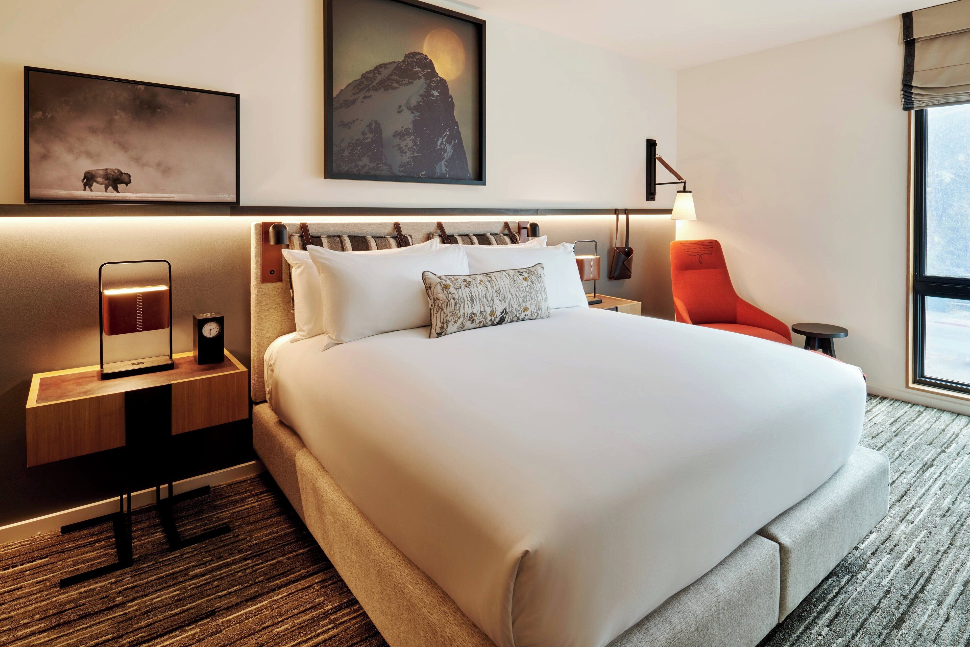 A hotel room with a large bed, a nightstand with a lamp, a chair, and artwork on the walls.
