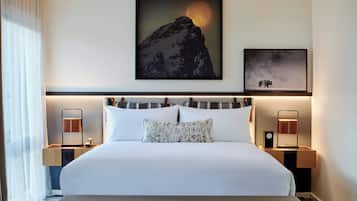 Une chambre d’hôtel avec un grand lit, deux tables de chevet, une œuvre d’art représentant une montagne accrochée au mur, et un tableau encadré représentant un bison.