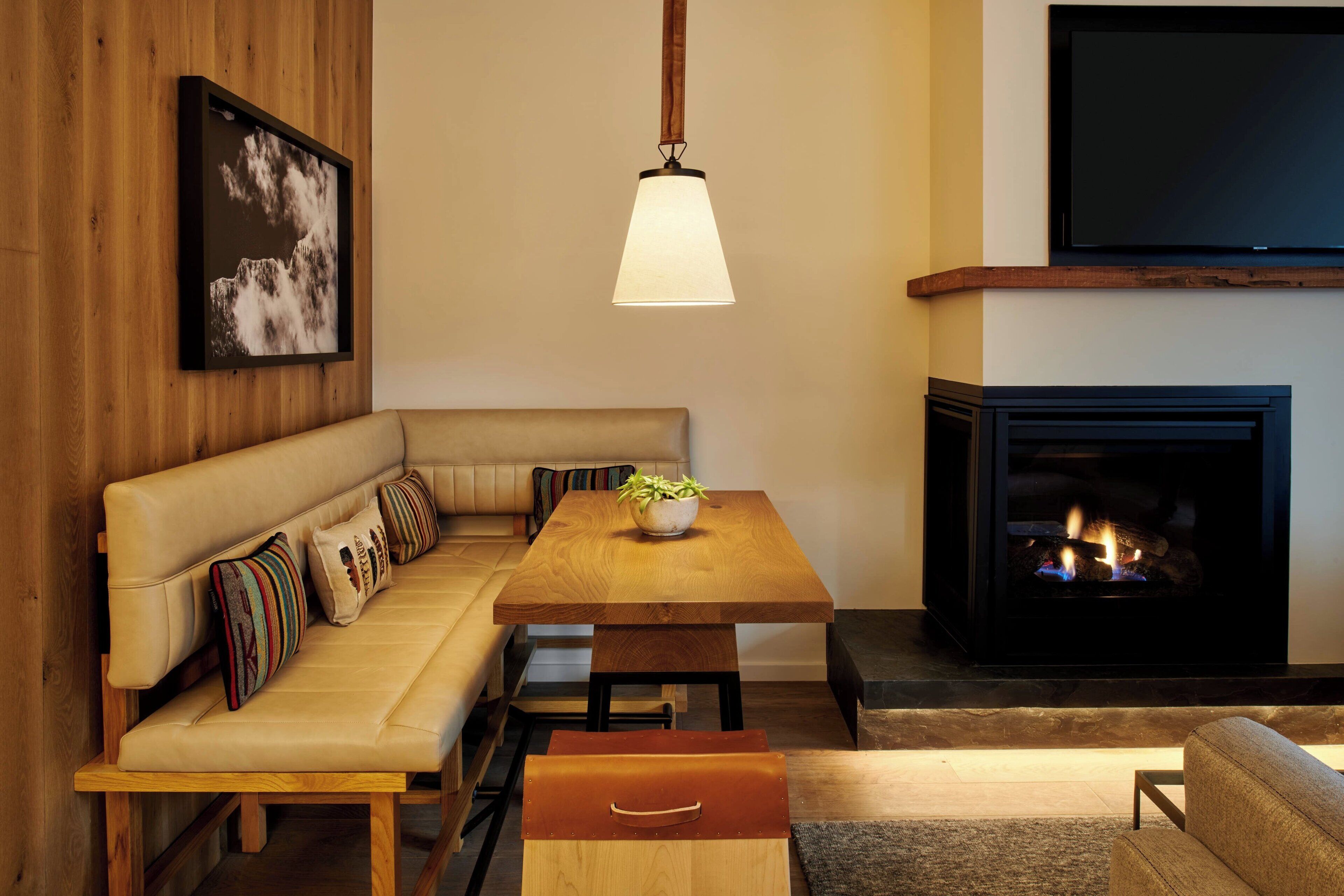 Ein gemütliches Wohnzimmer mit einem Holzsofa, einem Holzesstisch, einem Kamin und einem Wand-Fernseher.