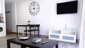 Una sala moderna con una mesa negra, dos sillas negras, un mueble blanco para entretenimiento y un gran reloj de pared.