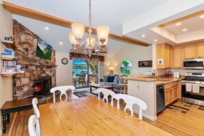 Een moderne keuken met een stenen open haard, houten keukenkastjes en een eethoek met een houten tafel en witte stoelen.