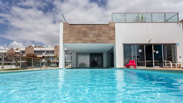 Un edificio moderno con piscina, zona cubierta y acceso de cristal.