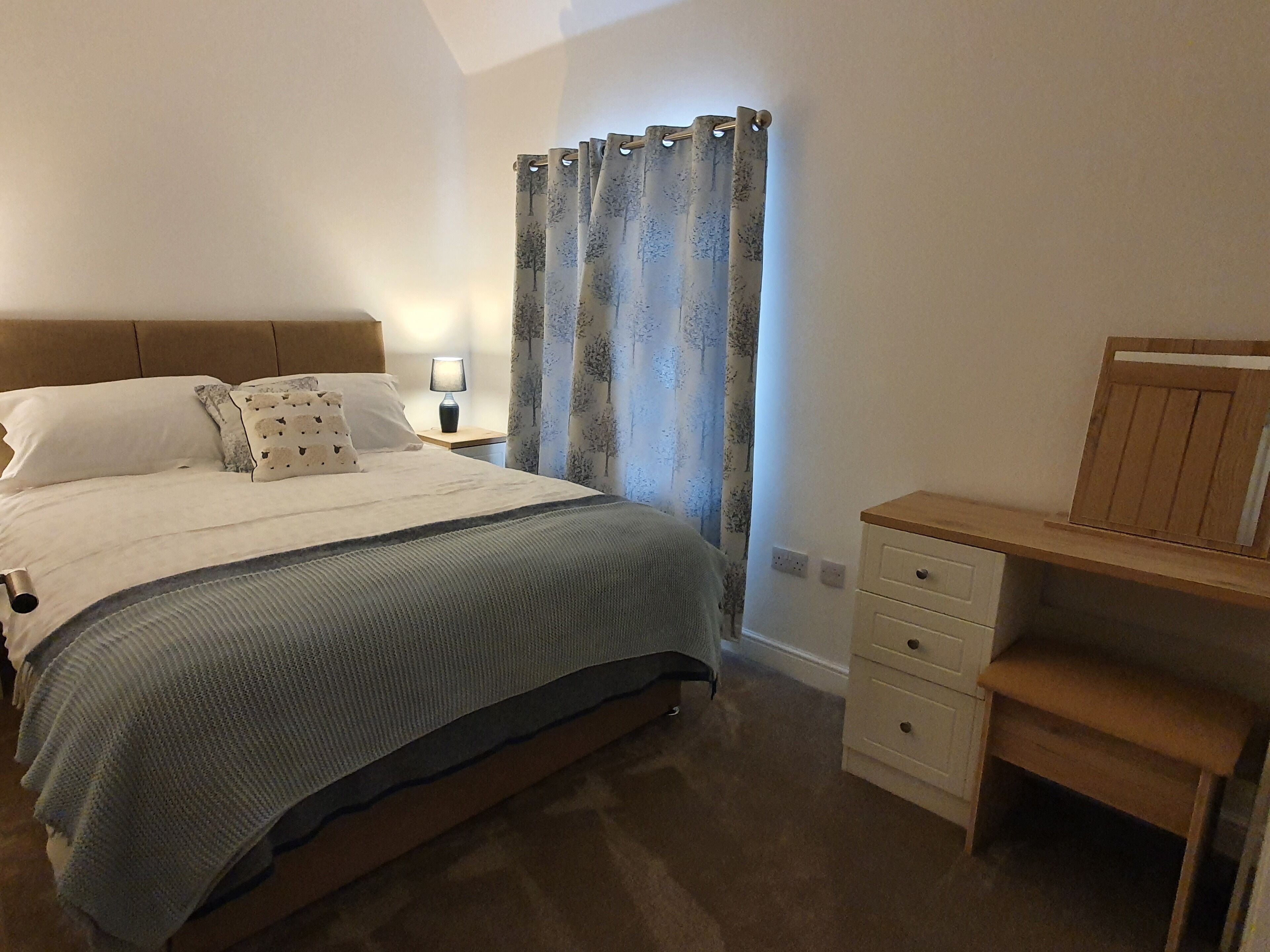 A bedroom with a bed, bedside table, lamp, and curtains.