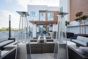 Een terras op het dak met buitenmeubilair, een pergola en een modern gebouw op de achtergrond.