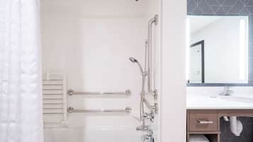 A modern bathroom with a white bathtub, a shower with a handheld showerhead, a glass-enclosed vanity with a mirror, and a towel rack.