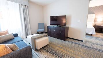A hotel room with a sofa, a TV, a small table, a bench, and a bed.