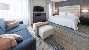 Une chambre d’hôtel avec un grand lit, un canapé, une télévision, un bureau et un sol recouvert de moquette.