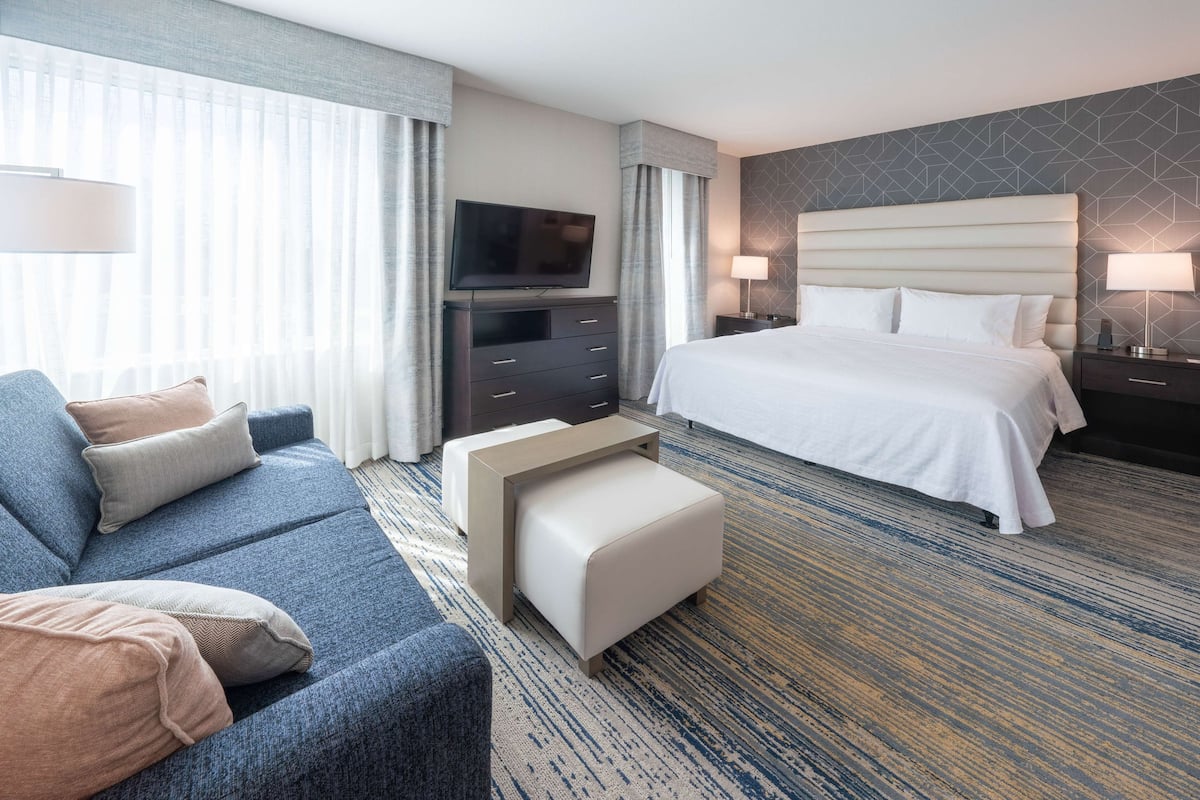 Ein Hotelzimmer mit einem großen Bett, einer Couch, einem Fernseher, einem Schreibtisch und einem Teppichboden.
