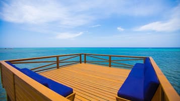 Une terrasse en bois avec des sièges rembourrés bleus, donnant sur un océan turquoise.