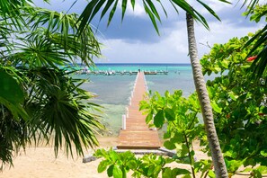 A wooden pier leading to a beach with clear turquoise water and boats.