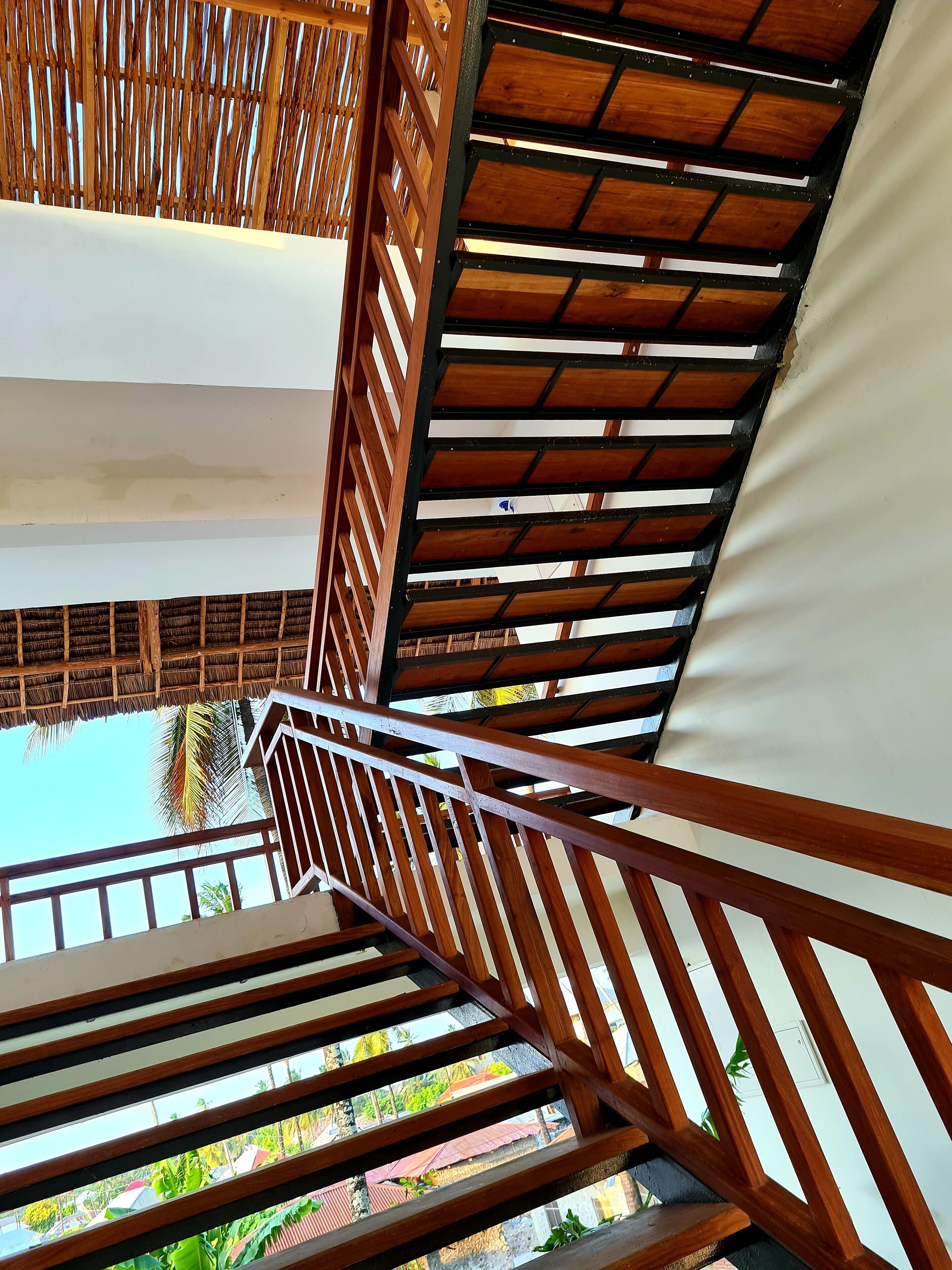 A wooden staircase with a metal handrail leading to a covered outdoor area.