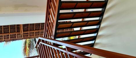 A wooden staircase with a metal handrail leading to a covered outdoor area.