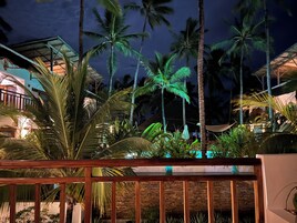 Vista nocturna de un complejo turístico con palmeras, una estructura de techo de paja y una valla de madera.