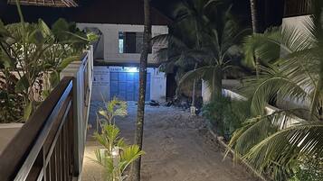 A nighttime view of a resort with a sandy pathway, palm trees, and a building with illuminated signage.