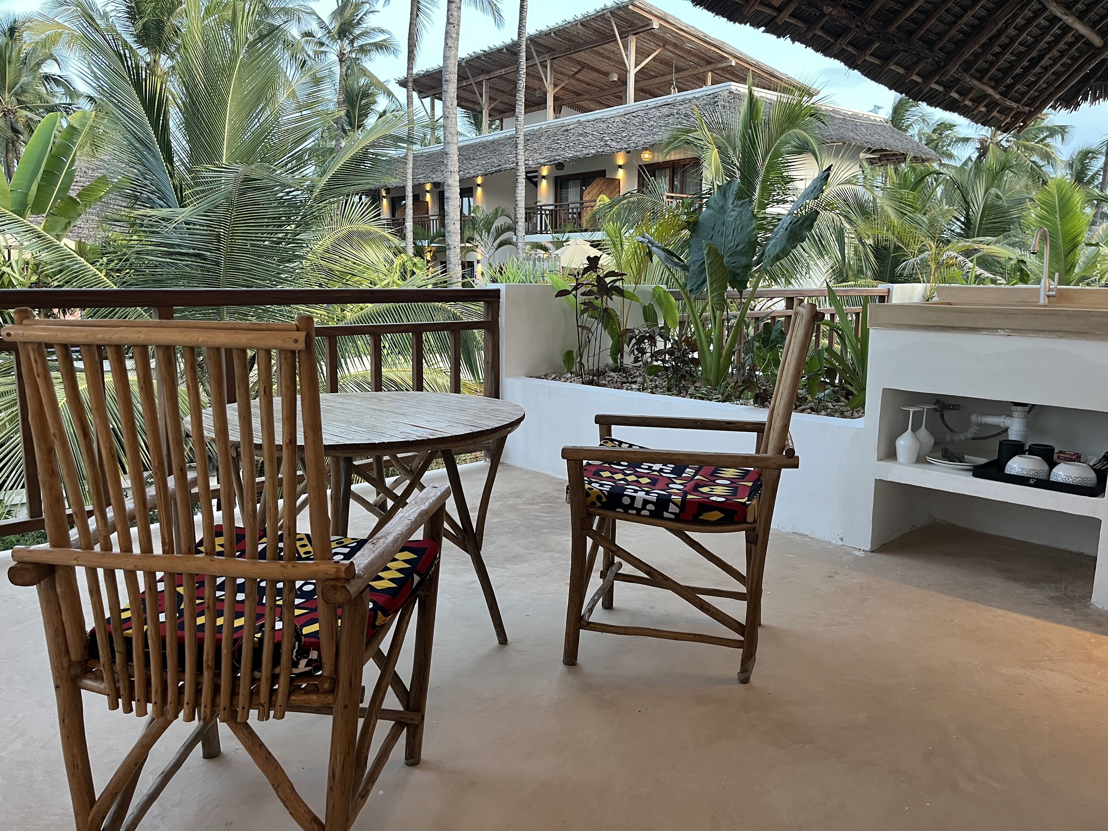 A wooden outdoor seating area with a table and chairs, surrounded by lush tropical plants.