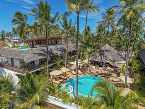 Un resort con piscina rodeada de palmeras y construcciones de techo de paja.
