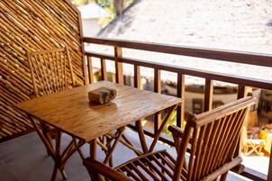 A wooden table and chairs on a balcony with a thatched roof in the background.